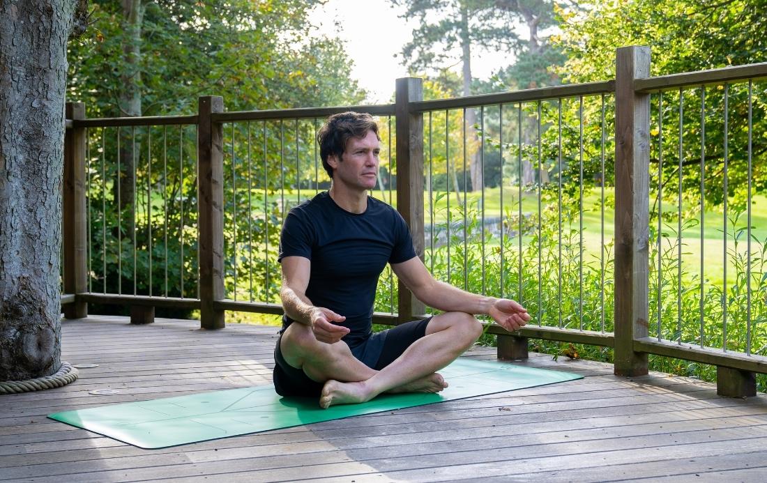 A man meditating on a yoga mat outside.